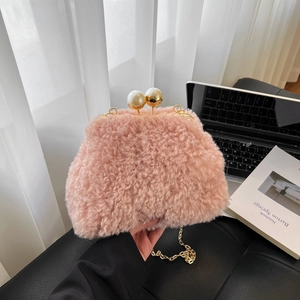 Pink plush crossbody bag with pearl clasp and gold chain strap in a cozy room
