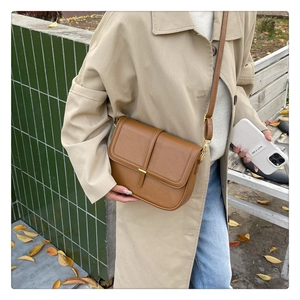 Detail of caramel leather crossbody bag worn with a beige trench coat in autumn setting