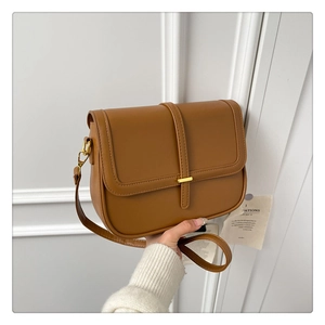 Detail of minimalist brown crossbody bag featuring a golden buckle and leather texture