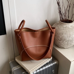 Brown litchi grain leather tote bag with white stitching on silver suitcase and books