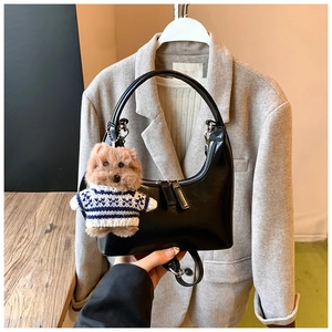 Detail of black crescent handbag with silver double zippers and plush puppy charm