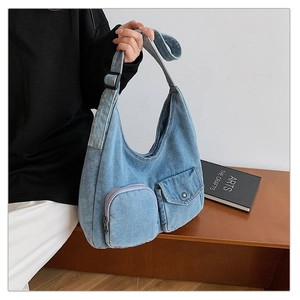 Detail of light blue denim shoulder bag showing dual pockets and washed texture