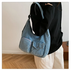Detailed close-up of blue denim shoulder bag featuring utility pockets and metal buttons
