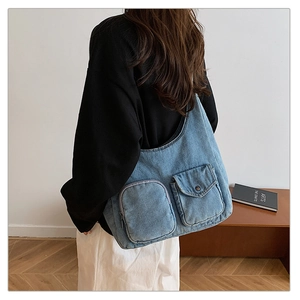 Detail of blue denim crossbody bag featuring large front pockets and contrast stitching