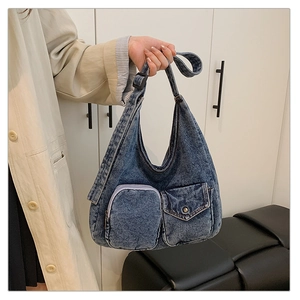 Detail of blue denim hobo bag featuring utility front pockets and adjustable strap