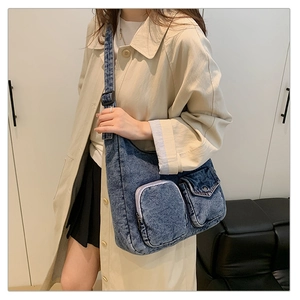 Close-up of blue washed denim crossbody bag with dual exterior pockets on beige coat