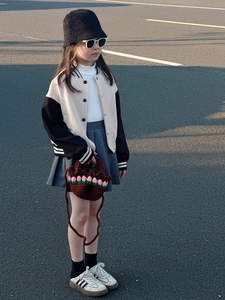 Detail of a brown flower crochet handbag paired with a kid's baseball jacket and pleated skirt