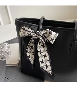 Detail of a black leather tote bag featuring a chic houndstooth ribbon handle decoration