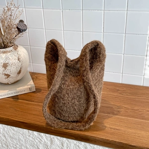 Brown fuzzy plush bucket bag with top handles shown in a cozy minimalist home setting