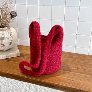 Red plush bucket bag with wide handle on a wooden surface for autumn winter style