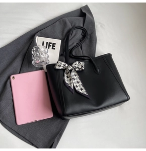 Close-up of black leather tote bag featuring a stylish houndstooth bow on the handle