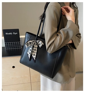 Detail of large black leather tote bag featuring a chic houndstooth bow charm and long straps