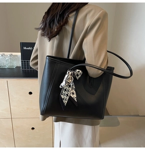 Large black leather tote bag with houndstooth ribbon shown on a model in a warm room