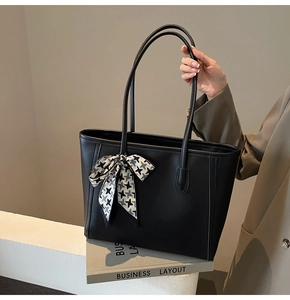 Close-up of black leather tote bag with houndstooth ribbon detail on business book