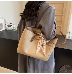 Detail of beige tote bag with houndstooth ribbon and dark brown straps on a model