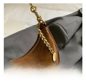Detailed view of brown wrinkled leather handbag with gold chain and circular metal pendant