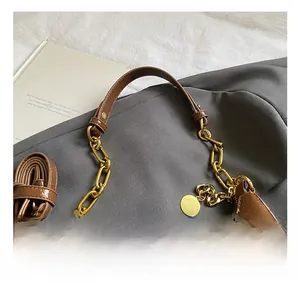 Detail of brown patent leather dumpling bag with gold chain and round metallic charm