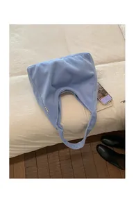 Detail shot of a soft light blue faux fur hobo bag placed on a cozy white bed background