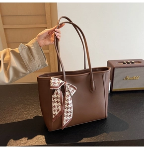Detail of dark brown tote bag with houndstooth bow handle held in a retro setting