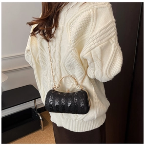Detail of black sequined evening clutch with gold metal handle and chain strap on sweater