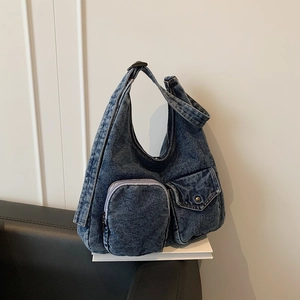 Retro washed dark blue denim shoulder bag with dual front pockets on a white book
