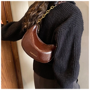 Detail of dark brown crescent bag with glossy leather texture and gold chain strap