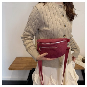 Detail of burgundy suede crossbody bag with wide strap worn with beige cardigan