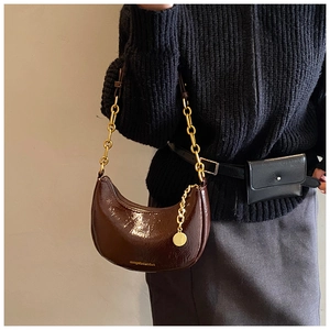 Detail of dark brown patent leather hobo bag with glossy finish and gold chain strap