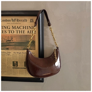 Detail of dark brown patent leather crescent bag with vintage texture and gold chain strap