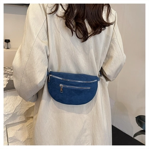 Rear view of model wearing a dark blue suede waist bag with adjustable strap and silver zippers
