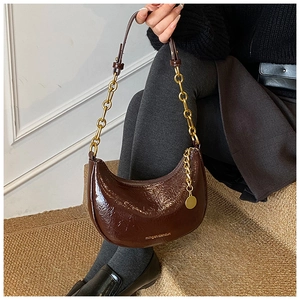 Detail of dark brown glossy hobo bag with gold chunky chain and metallic pendant