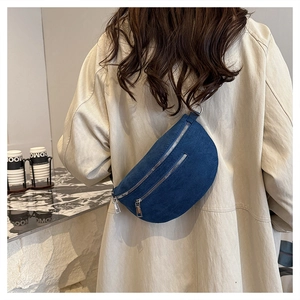 Detail of blue denim crescent belt bag worn over a beige coat with silver zippers
