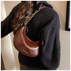 Detail of dark brown crescent bag featuring crinkled texture and gold chain strap