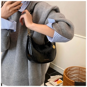 Detail view of glossy black crescent shoulder bag with golden hardware and chain accents