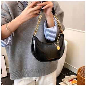 Detail of black semi-circle bag with glossy crinkle leather and chunky gold chain strap