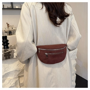 Detail of dark brown suede fanny pack with silver zippers styled on a beige long coat