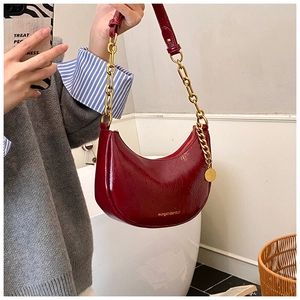Detail of burgundy patent leather hobo bag with gold chain strap and metal pendant