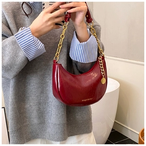 Detail view of burgundy hobo bag featuring bold gold chain strap and metal logo tag