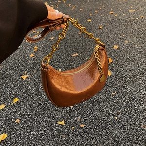 Detail of warm brown leather crescent bag with golden chain and vintage texture