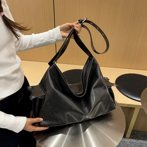 Detail of a large black soft leather tote bag with metal eyelet accents and wide shoulder strap