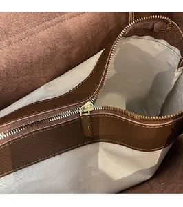 Dettaglio borsa in pelle marrone con cerniera dorata e fodera in tessuto a spina di pesce