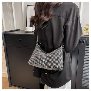 Silver rhinestone hobo bag with black leather handle and chain strap shown in a modern setting
