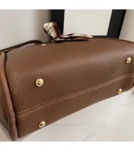 Dettaglio della base della borsa in pelle marrone con borchie dorate e cuciture