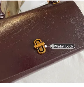 Detailed close-up of dark wine red leather texture and golden oval hardware clasp on handbag