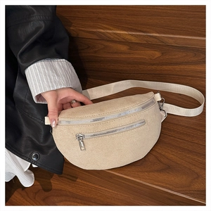 Detail of beige suede crescent bag with dual silver zippers and adjustable strap