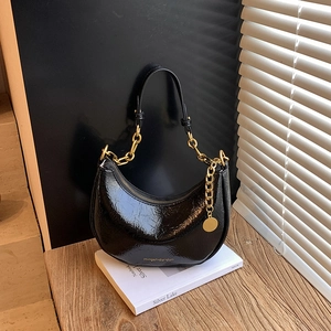 Detail of glossy pleated leather texture with gold chain on a black crescent hobo bag