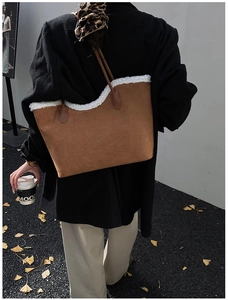 Detail of brown suede tote bag featuring white faux shearling trim and slim leather handles