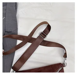 Close-up of brown suede crossbody bag with wide nylon strap and silver metal hardware