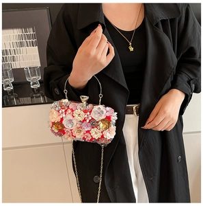 Detail of red floral evening bag featuring 3D flowers and golden metal handle held by model