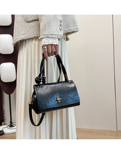 Close-up of black textured leather bag with gold oval twist lock and knot handle
